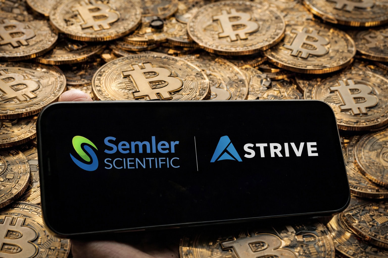Ein Smartphone-Bildschirm zeigt die Logos von Strive und Semler Scientific. Im Hintergrund sind Bitcoin-Münzen.