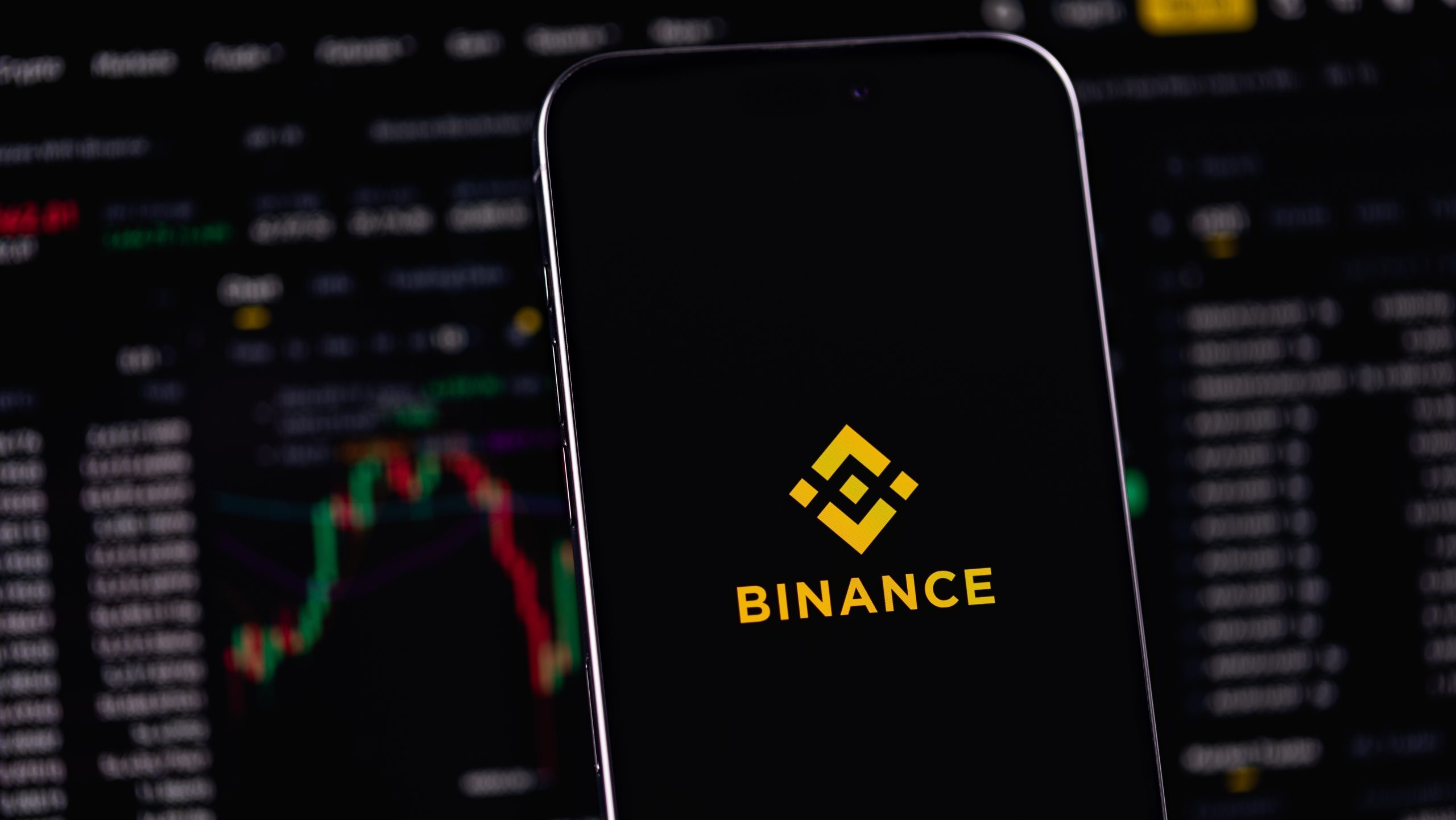 Smartphone mit Binance-Logo vor einem Trading-Interface