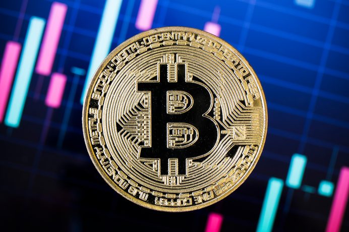 Eine Bitcoin-Münze vor einem Kurschart