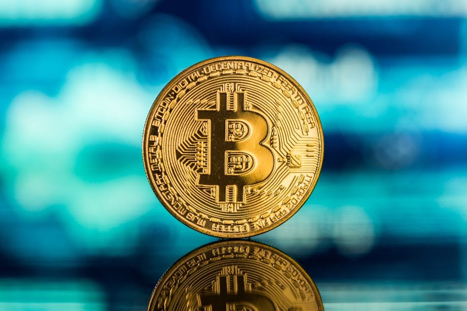 Eine Bitcoin-Münze vor einem Kurschart
