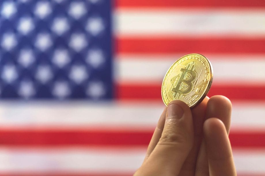 Hand hält Bitcoin-Coin vor US-Flagge als Symbolbild für Bitcoin in US-Altersvorsorgeplänen