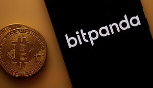 Bitpanda Logo auf dem Bildschirm eines Smartphones neben einer Bitcoin Münze.