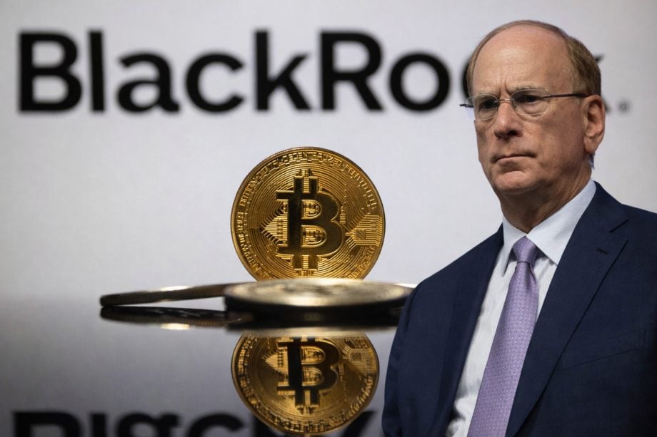 Mann im Anzug steht rechts im Bild vor unscharfem BlackRock-Schriftzug. Im Vordergrund ist eine goldene Bitcoin-Münze auf einer reflektierenden Oberfläche zu sehen. Symbolische Darstellung von Bitcoin, institutionellen Investoren und Finanzmärkten.