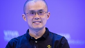 CZ mit Brille und schwarzem Binance-Poloshirt lächelt vor einem lilafarbenen Hintergrund mit Binance-Motiven.