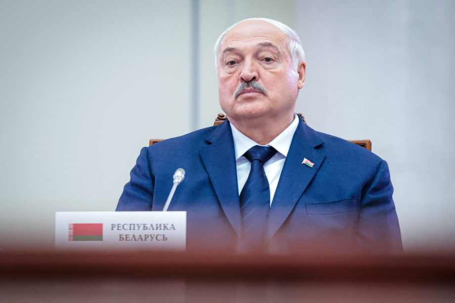 Alexander Lukaschenko im marineblauen Anzug sitzt vor einem Mikrofon.