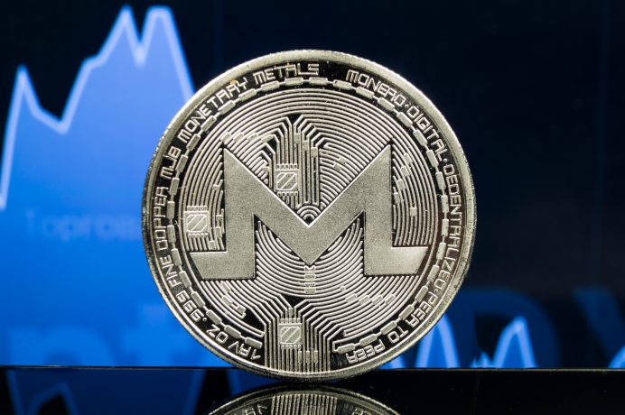 Eine Symbolmünze der Kryptowährung Monero vor einem blau gefärbten Kurschart