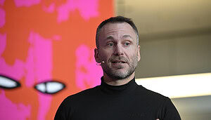 Ein Mann mit schwarzem Rollkragenpullover hält eine Rede.