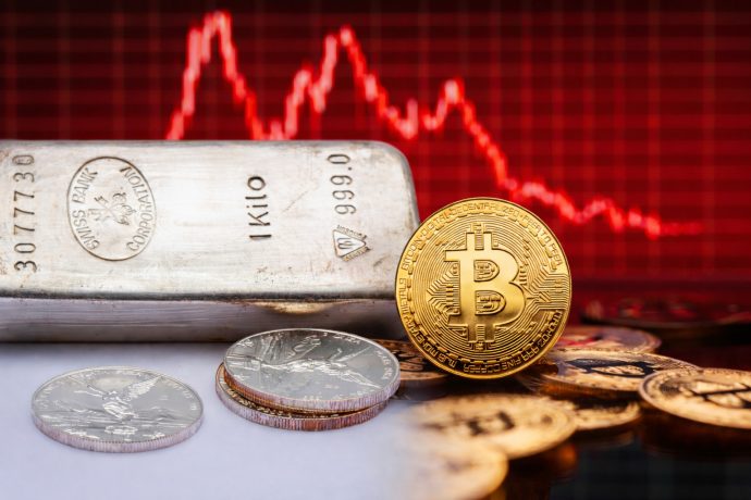 Ein Silberbarren und eine Bitcoin-Münze vor einem rötlichen Chart.
