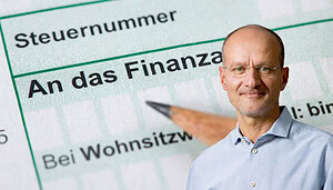 Montage mit einem Steuerformular mit der Aufschrift „An das Finanzamt“ im Hintergrund und einem Mann im hellblauen Hemd im rechten unteren Bildbereich. Das Bild steht symbolisch für das Thema Steuer, Steuererklärung und steuerliche Pflichten.
