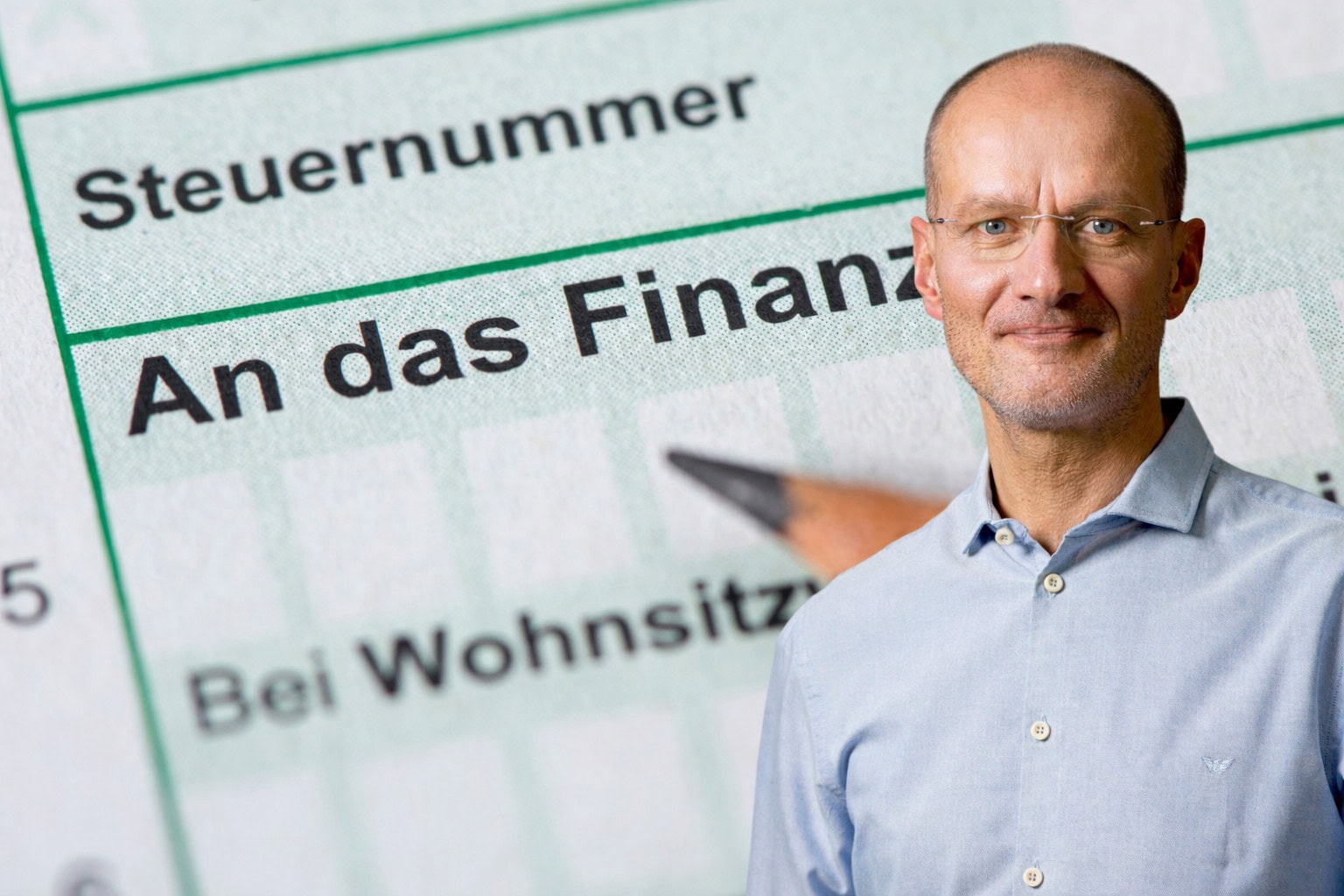 Mann mit Brille und hellblauem Hemd steht rechts im Vordergrund. Im Hintergrund ist ein deutsches Steuerformular mit den Aufschriften ‚Steuernummer‘ und ‚An das Finanzamt‘ sowie ein angespitzter Bleistift zu sehen. Symbolbild für Krypto-Steuern, Steuererklärung und steuerliche Behandlung von Kryptowährungen.