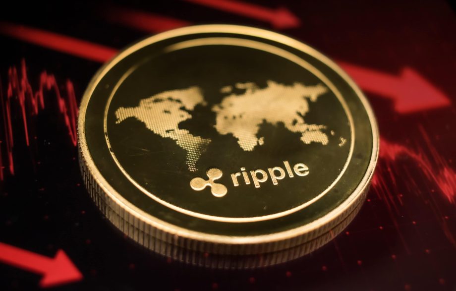 Eine goldene XRP-Münze mit dem Ripple-Logo und einer Weltkarte ruht auf einer dunklen Oberfläche, die von roten Finanzdiagrammlinien beleuchtet wird.