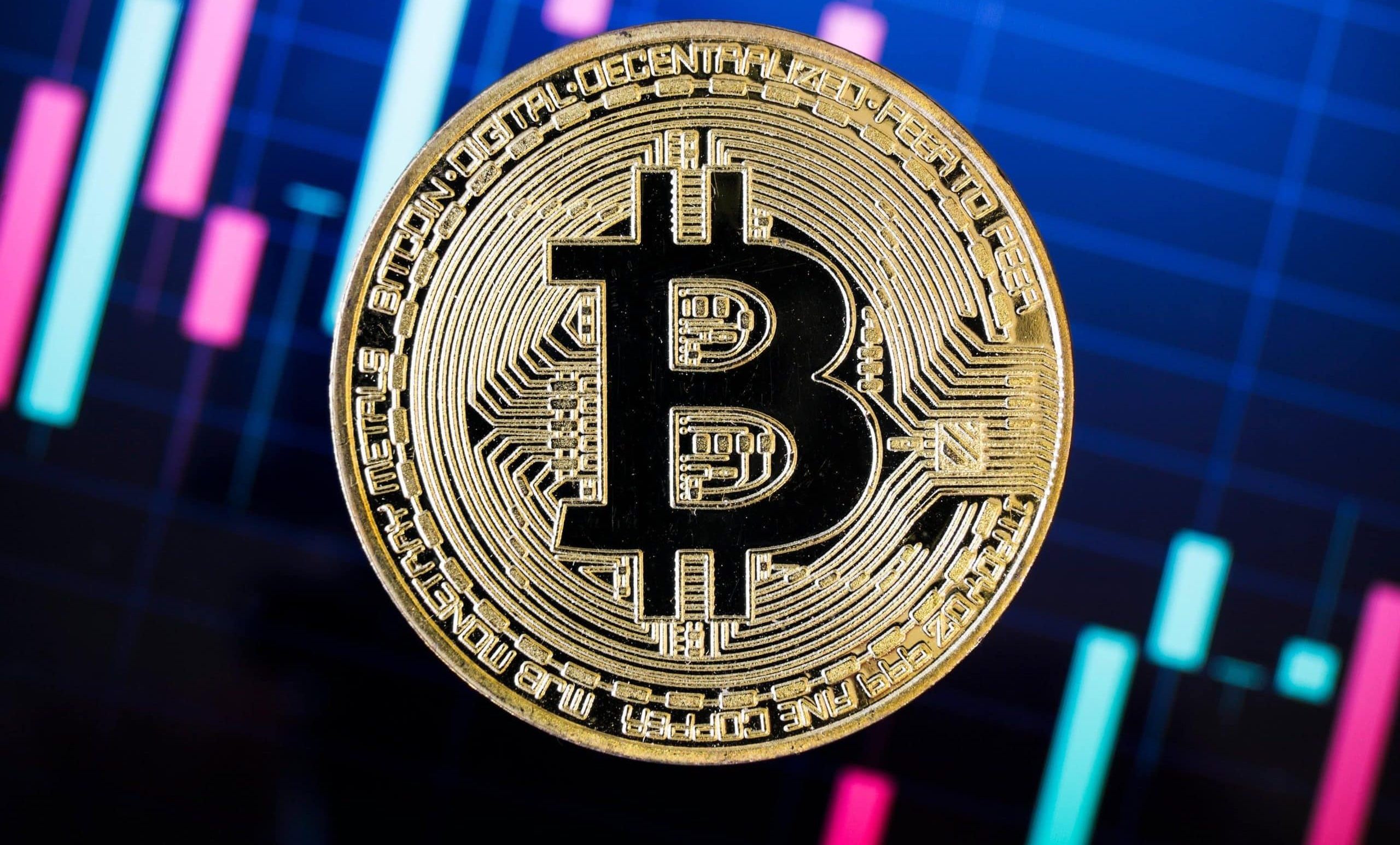 Eine Bitcoin-Münze vor einem Kurschart.