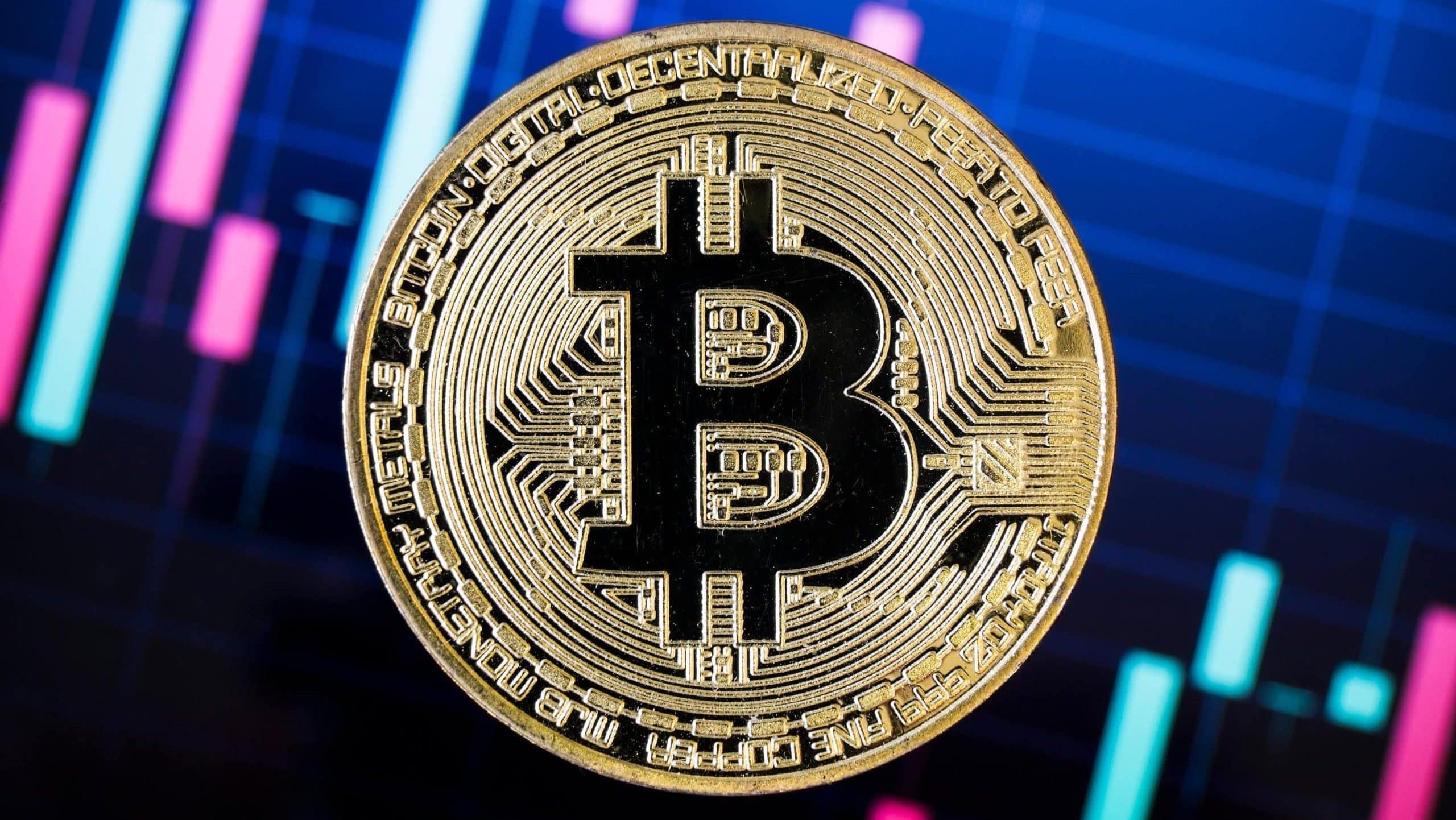 Eine Bitcoin-Münze vor einem Kurschart.