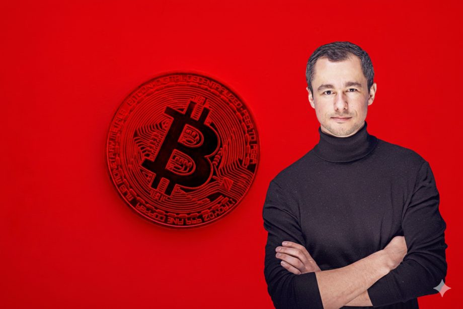 Eine Bitcoin-Münze vor einem roten Hintergrund. Rechts am Bild steht ein Mann mit schwarzem Rollkragenpullover.