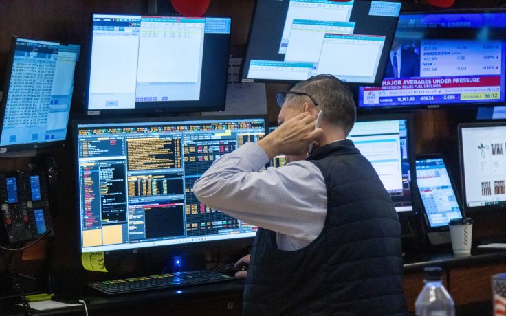 Ein Trader sitzt vor seinem Schreibtisch, starrt auf mehrere Bildschrime und kratzt sich am Nacken.