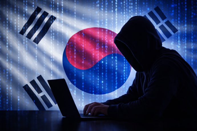 Bitcoin Hack Südkorea: Vermummter Hacker am Laptop vor Südkorea-Flagge mit Binärcode-Hintergrund