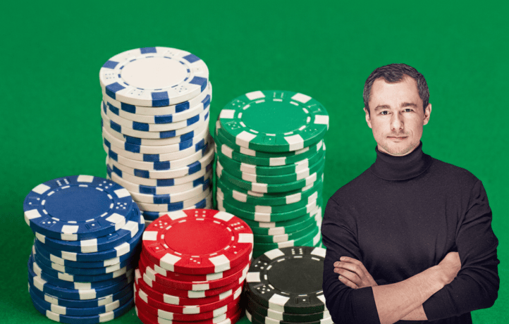 Mehrere bunte Pokerchips sind vor einem grünen Hintergrund in Stapel aufgeteilt. Rechts auf dem Bild steht ein Mann mit schwarzem Rollkragenpullover.