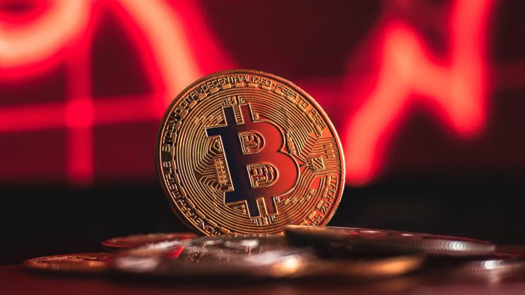 Bitcoin-Münze vor rotem Hintergrund, der einen fallenden Kurs symbolisiert