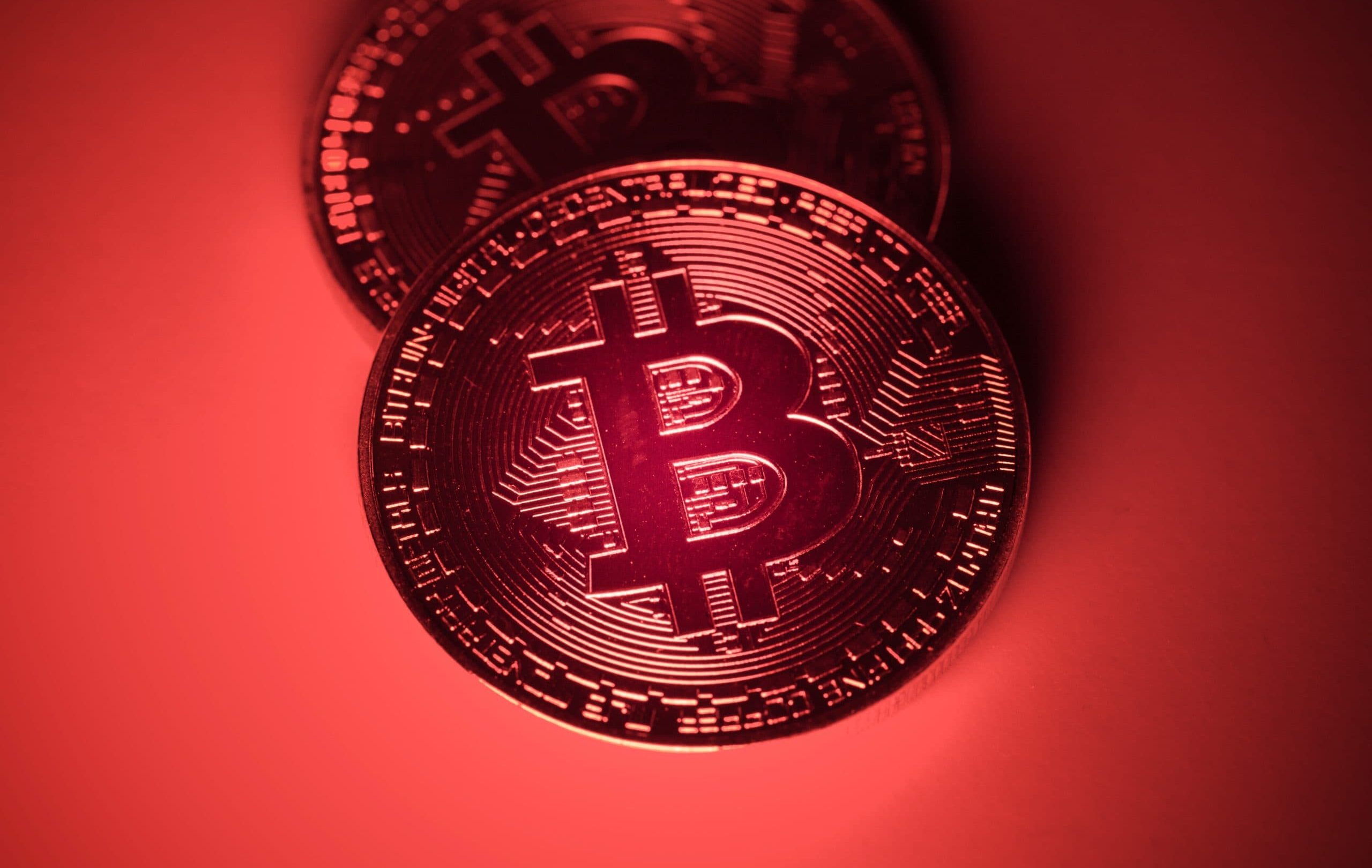 Zwei physische Bitcoin-Token (BTC) werden unter rotem Licht gezeigt, wobei auf ihrer Oberfläche kreislaufähnliche Muster zu erkennen sind, die das digitale Wesen von Bitcoin hervorheben.