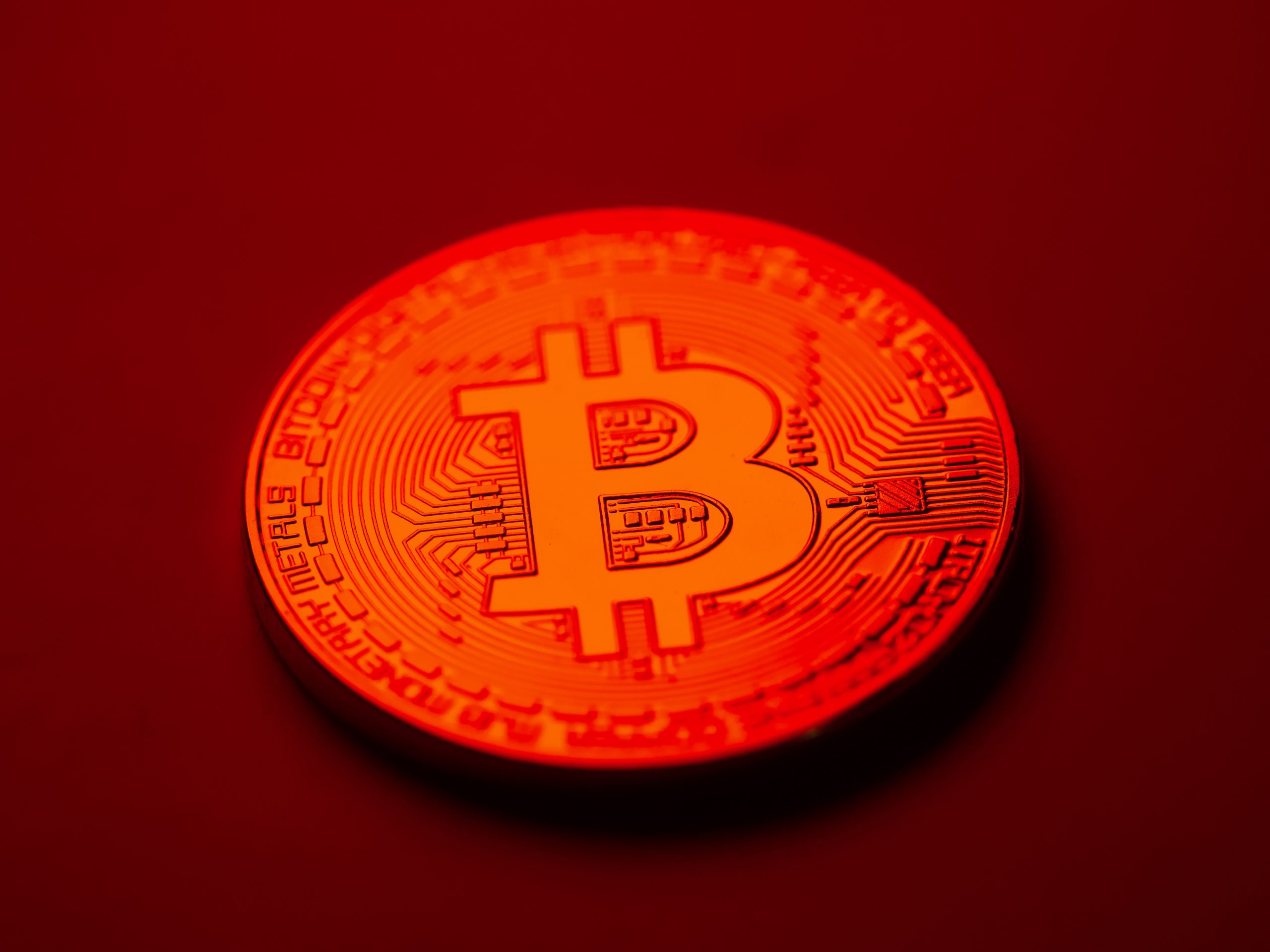 Eine rote Bitcoin-Münze liegt auf einem roten Hintergrund