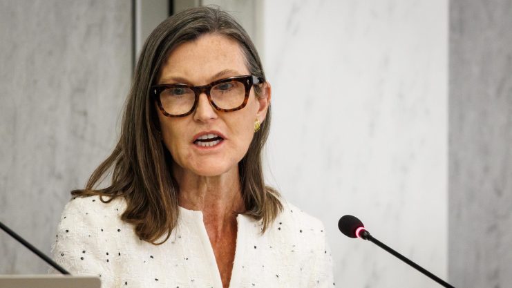 Cathie Wood legt nach Eine Frau mit Brille und feiner Bluse vor einem Mikrofon.