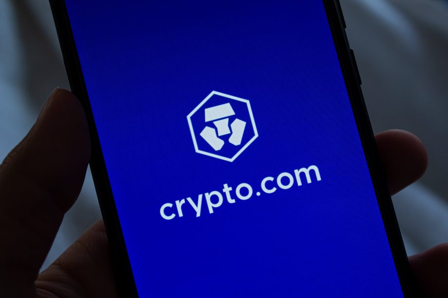 Crypto.com-Schriftzug auf blauem Hintergrund, von einer Hand gehalten.