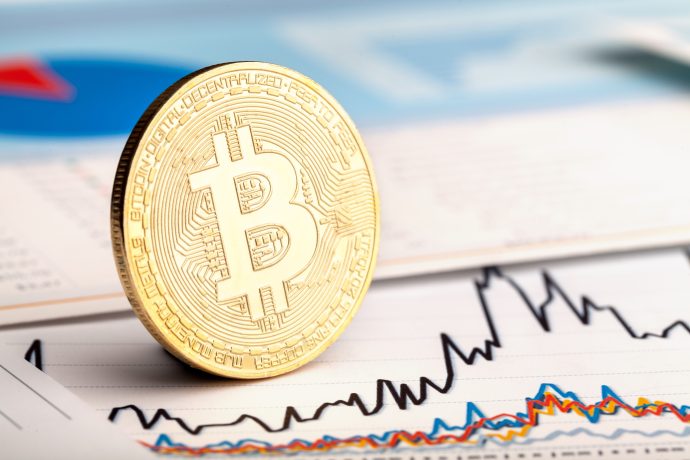 Eine Bitcoin-Münze steht aufrecht auf einer Zeitung