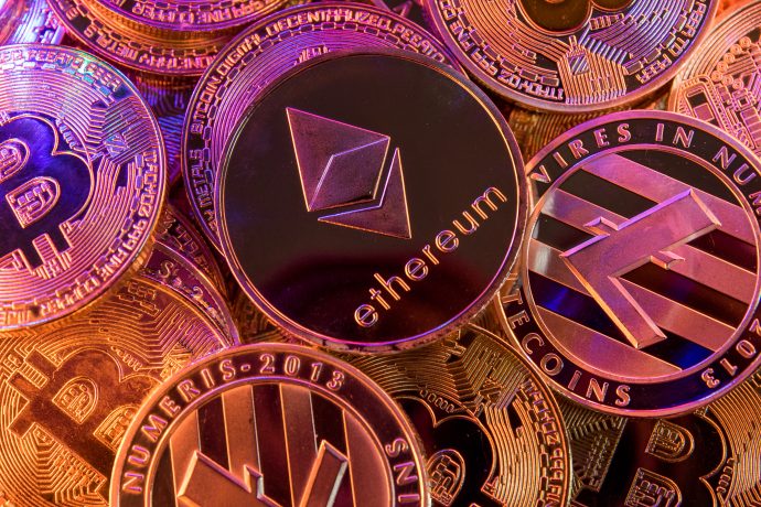 Mehrere aufeinander und rot ausgeleuchtete Münzen von Kryptowährungen wie Bitcoin und Ethereum