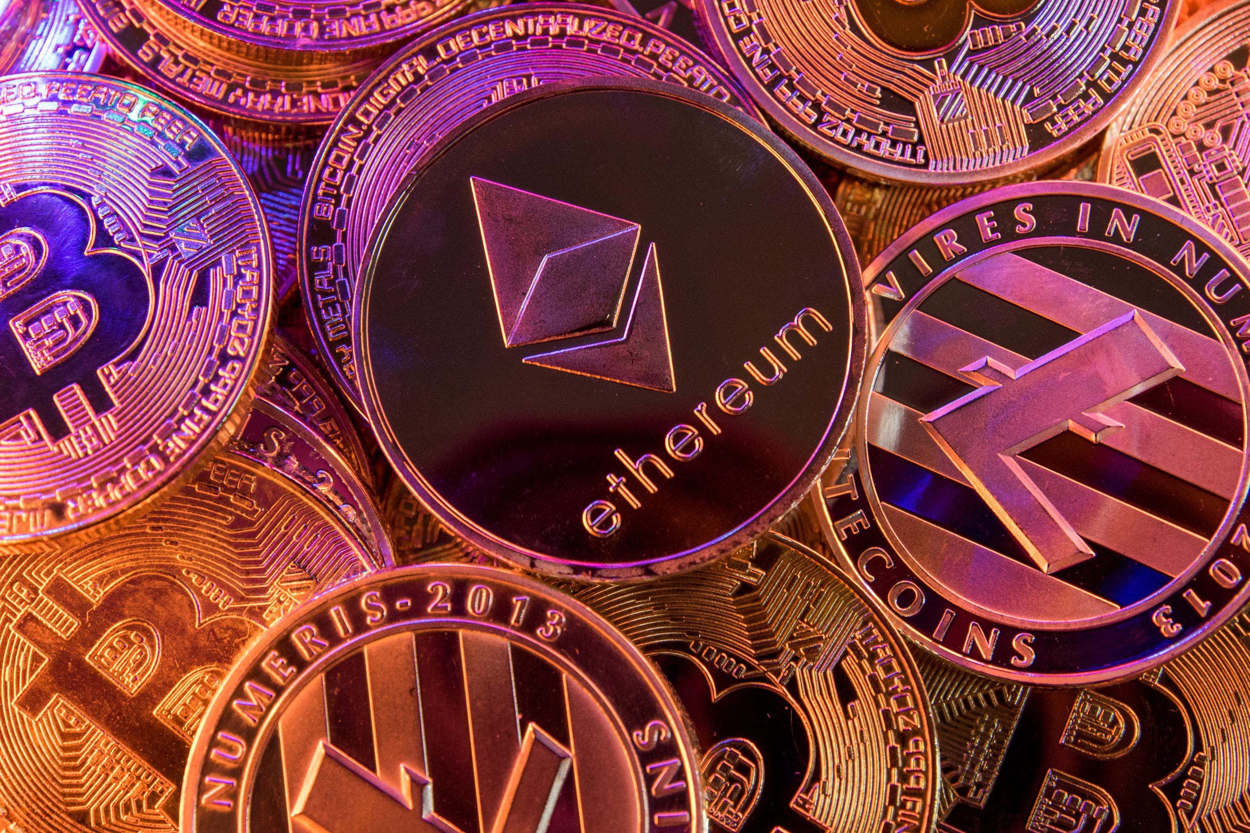 Mehrere aufeinander und rot ausgeleuchtete Münzen von Kryptowährungen wie Bitcoin und Ethereum