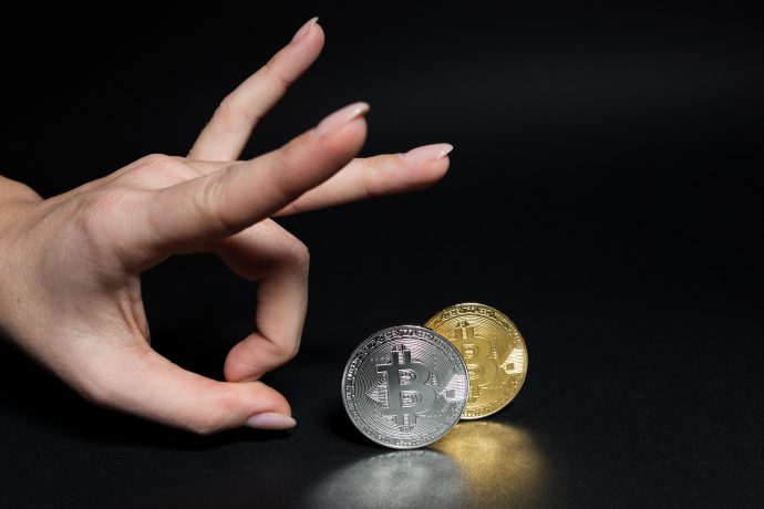Eine Hand flippt eine Bitcoin-Münze vor einem schwarzen Hintergrund