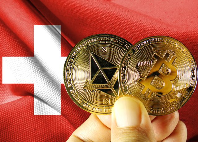 Eine Hand hält Bitcoin-Münzen vor einer Schweizer Flagge