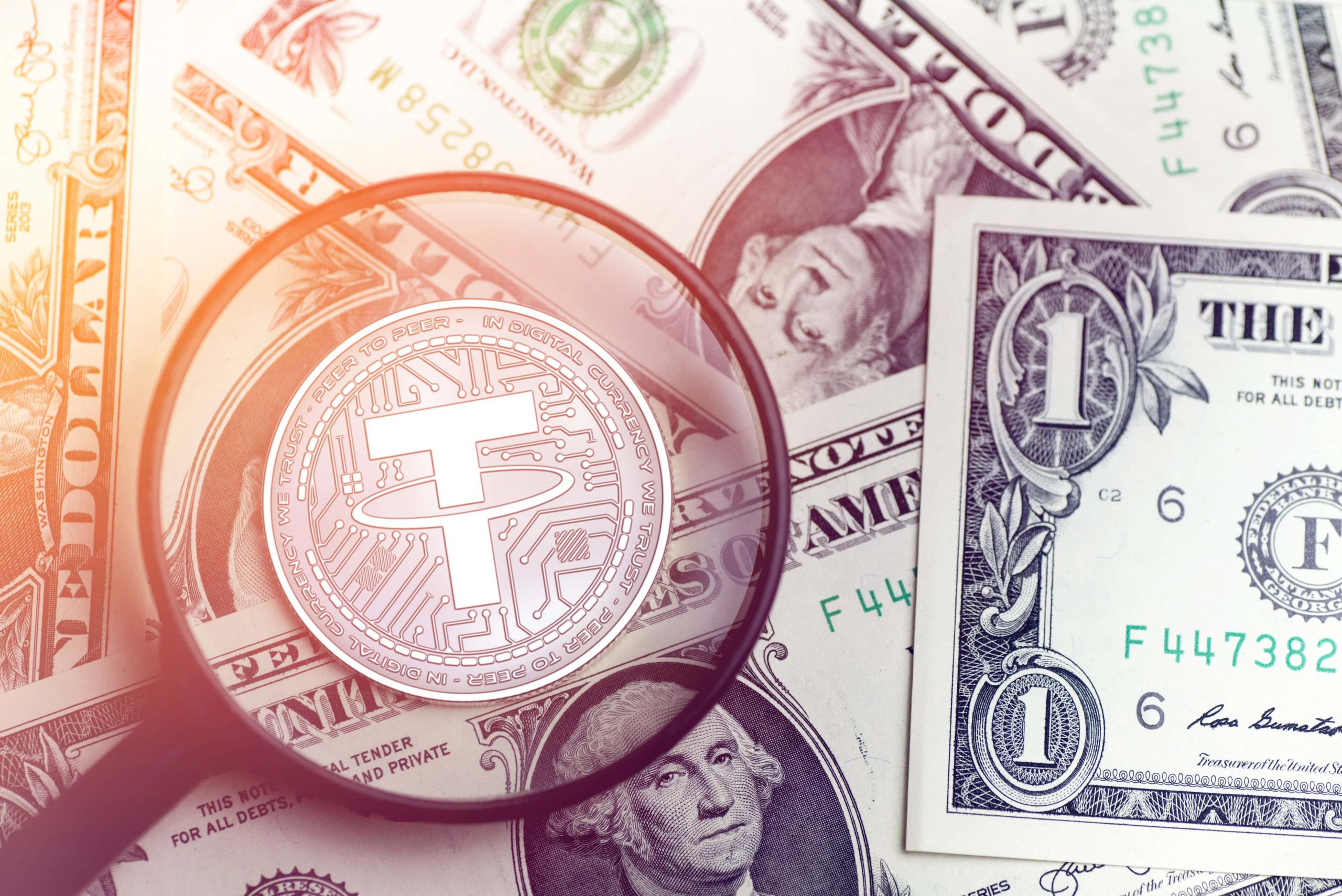 Eine Lupe zeigt auf den US Stablecoin Tether (USDT), der auf einem Stapel Dollarscheinen liegt.