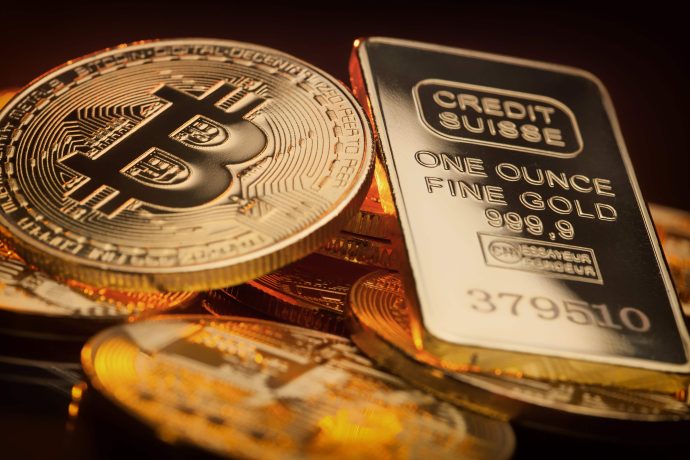 Eine Bitcoin-Münze liegt neben einem Goldbarren