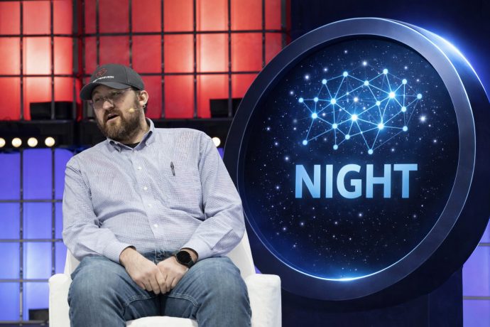 Charles Hoskinson sitzt auf einer Bühne, neben ihm ein groß dargestellter NIGHT-Token.