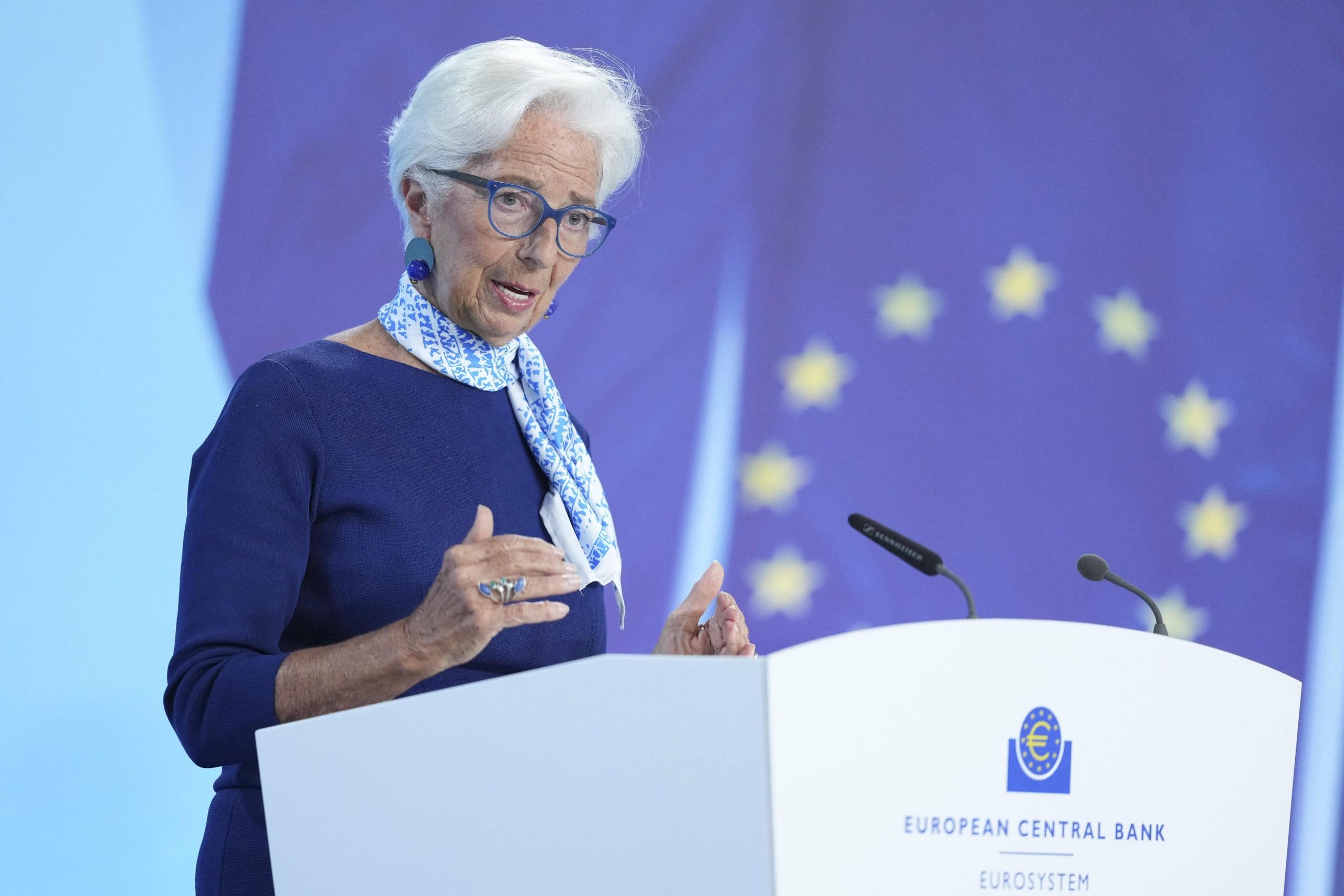Eine Frau mit kurzen weißen Haaren und Brille (Christine Lagarde) spricht an einem Podium mit der Aufschrift Europäische Zentralbank Eurosystem, im Hintergrund ist eine EU-Flagge zu sehen.