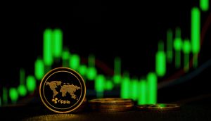 Eine Ripple XRP-Kryptowährungsmünze, die aufrecht vor gestapelten Münzen steht, mit einem grünen Candlestick-Kursdiagramm im unscharfen Hintergrund.