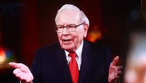 Ein älterer Mann im Anzug und mit roter Krawatte gestikuliert mit beiden Händen, während er während eines Interviews spricht und seine Erkenntnisse als Bitcoin-Experte mit Investoren teilt.