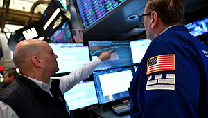 Das Bild zeigt die New York Stock Exchange, wie 2 Männer auf dem Bildschirm auf Polymarket schauen.