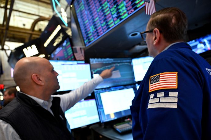 Das Bild zeigt die New York Stock Exchange, wie 2 Männer auf dem Bildschirm auf Polymarket schauen.