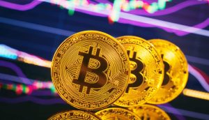 Drei Bitcoin-Münzen stehen aufrecht vor einem bunt gefärbtem Chart als Hintergrund