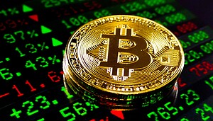 Das Bild zeigt eine Bitcoin-Münze auf einem Bildschirm mit Kurszahlen.