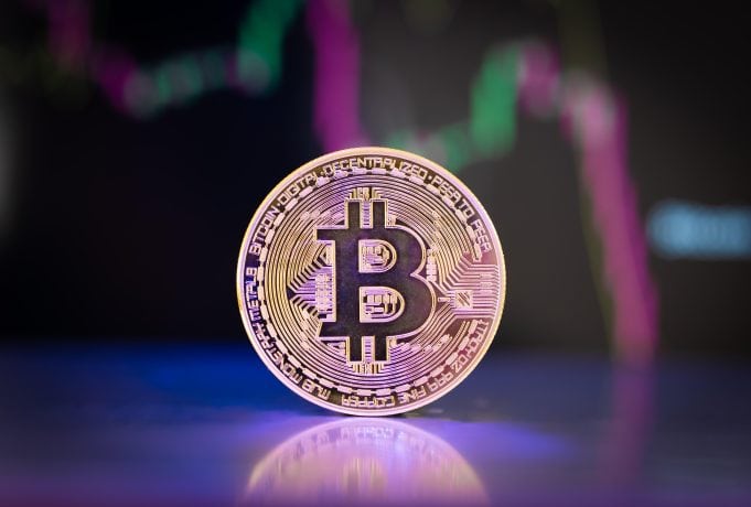 Eine Bitcoin-Münze vor einem fallenden Kurs-Chart.
