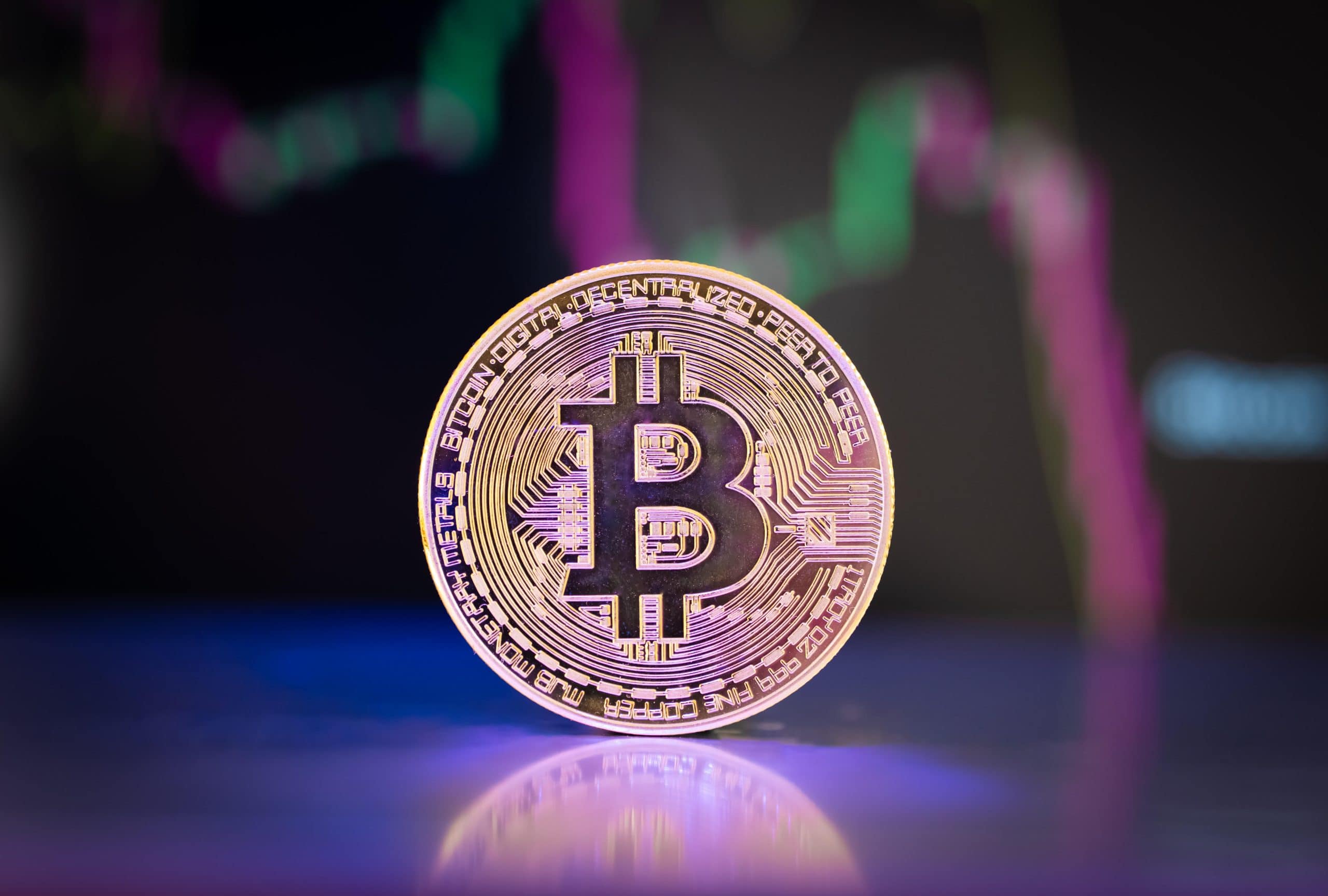Eine Bitcoin-Münze vor einem fallenden Kurs-Chart.