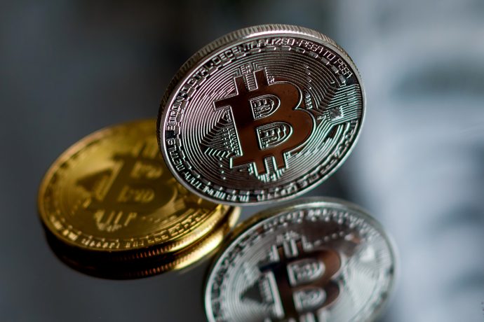 Eine aufrecht stehende Bitcoin-Münze vor einem verspiegelten Hintergrund