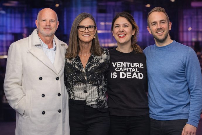 Das Bild zeigt vier Personen, die nebeneinander stehen und direkt in die Kamera lächeln, als würden sie gemeinsam für ein Event- oder Pressefoto posieren.