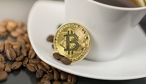 Eine Kaffeetasse, an die eine Bitcoin-Münze gelehnt ist