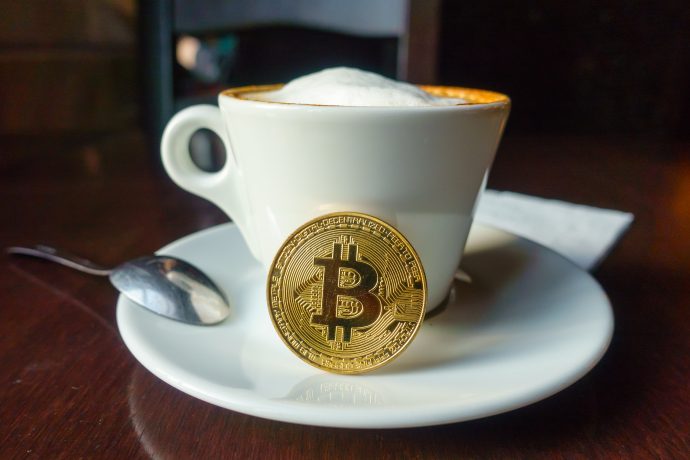 Eine Bitcoin-Münze angelehnt an eine Kaffee-Tasse