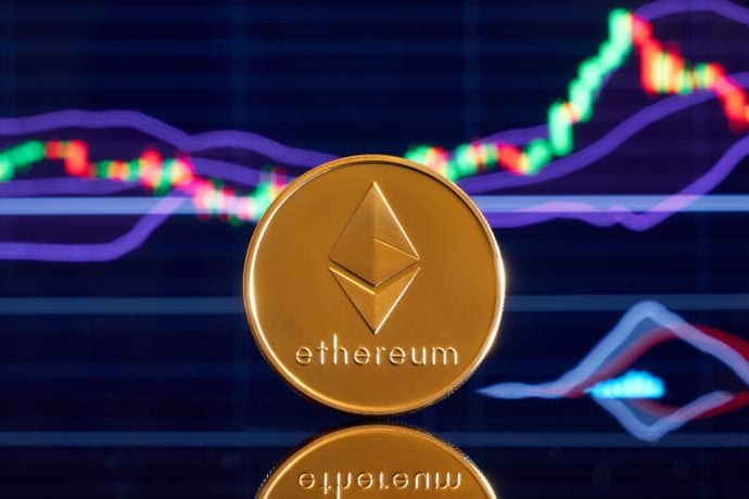 Eine physische Ethereum-Münze steht aufrecht vor einem digitalen Bildschirm, der schwankende Ethereum-Finanzcharts anzeigt.