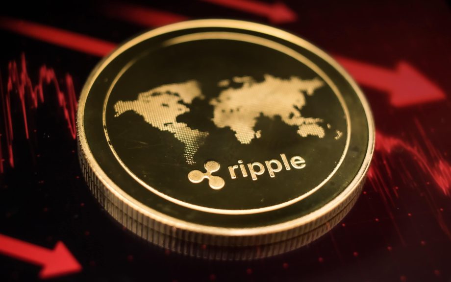 Eine goldene XRP-Münze mit dem Ripple-Logo und einer Weltkarte ruht auf einer dunklen Oberfläche, die von roten Finanzdiagrammlinien beleuchtet wird.