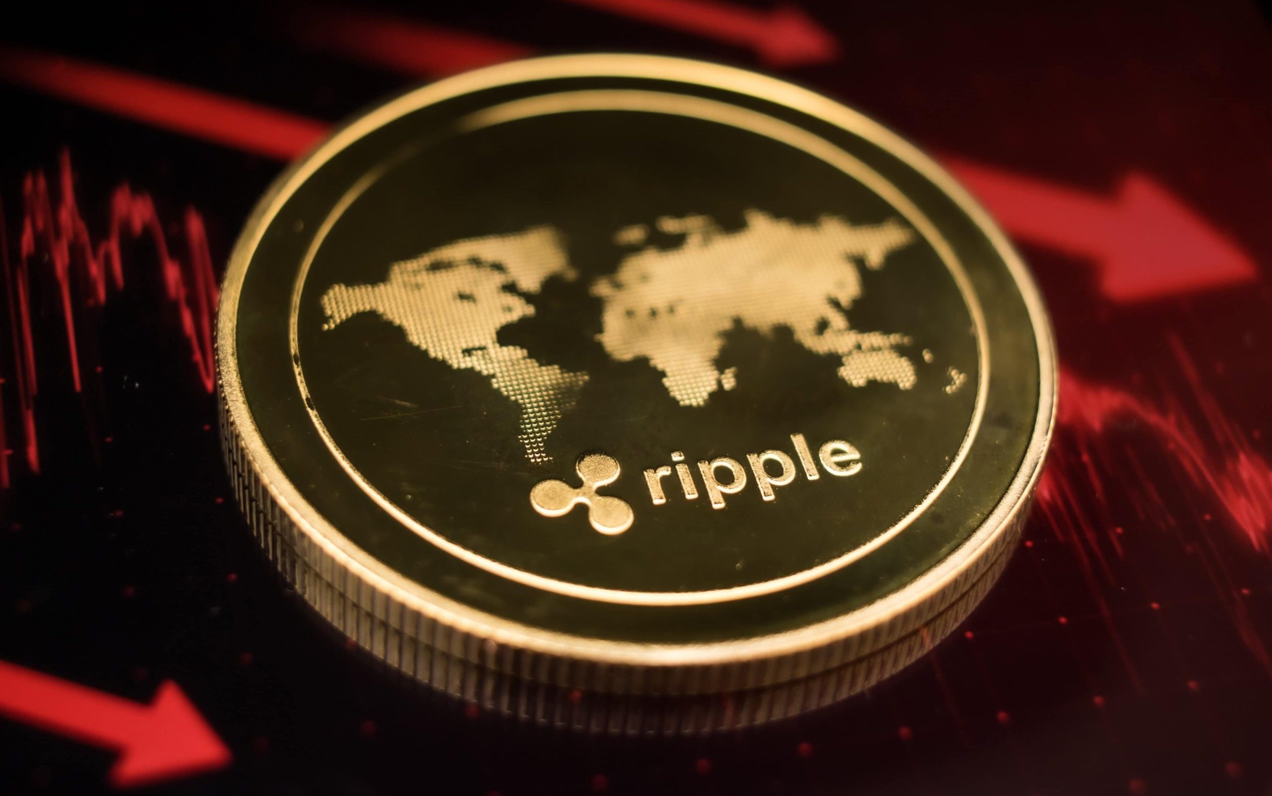 Eine goldene XRP-Münze mit dem Ripple-Logo und einer Weltkarte ruht auf einer dunklen Oberfläche, die von roten Finanzdiagrammlinien beleuchtet wird.